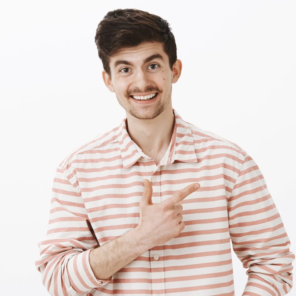 A smiling man with a mustache, wearing a pink and white striped shirt, pointing to the side