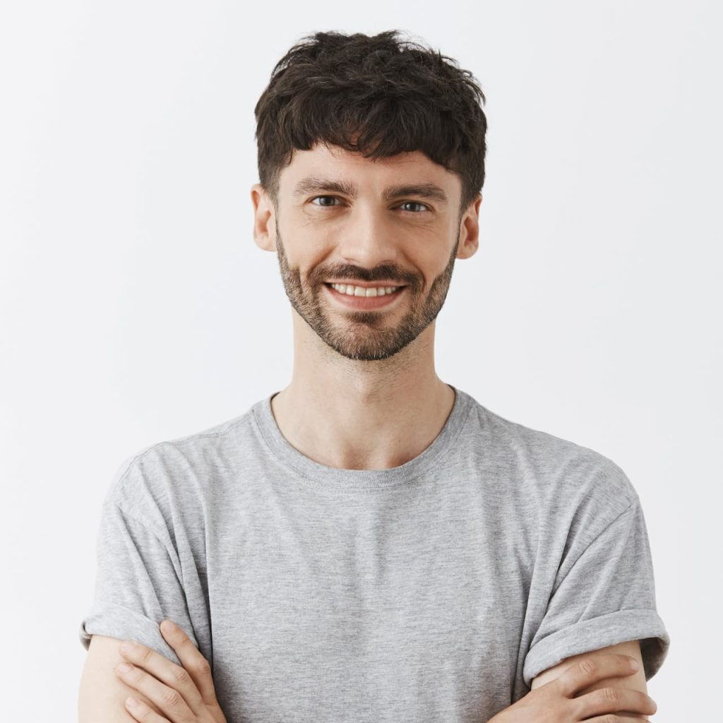 Smiling man in a gray T-shirt standing with his arms